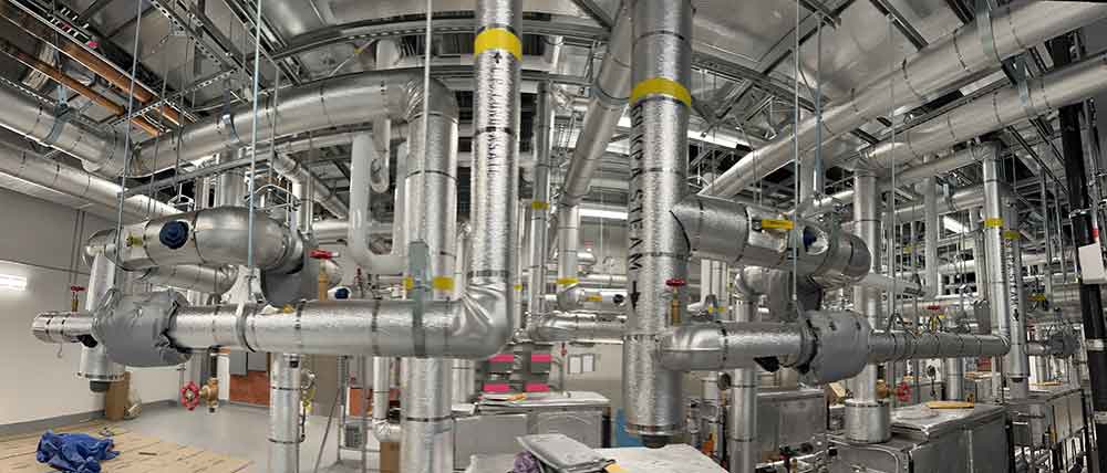 Commercial Mechanical Insulation System Installation Mechanical insulation installed on commercial piping systems and equipment in a large mechanical room.
