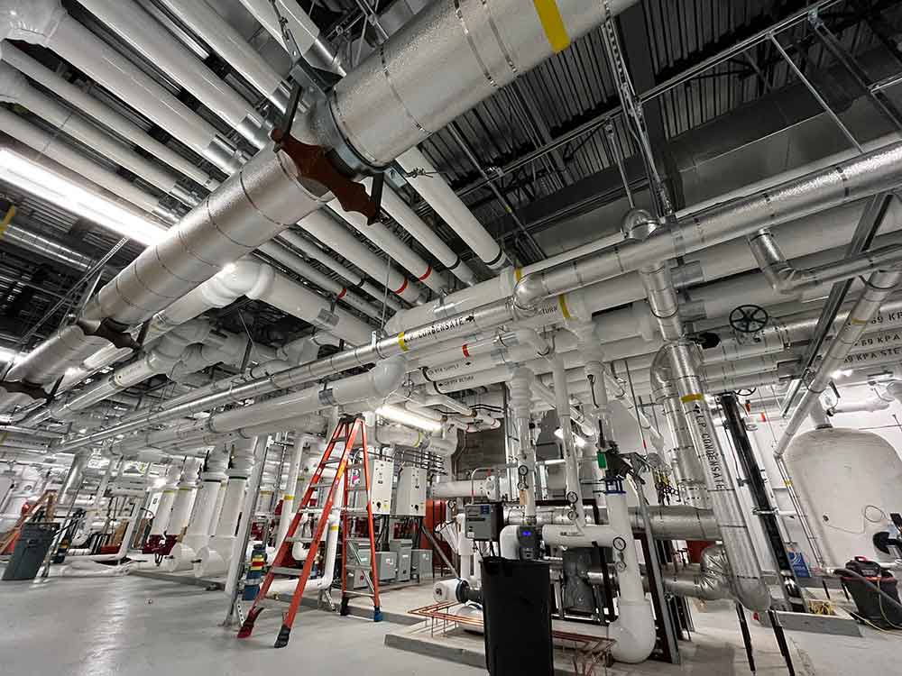 Commercial Mechanical Insulation in Mechanical Room Mechanical insulation installed on overhead piping and duct systems in a commercial mechanical room.